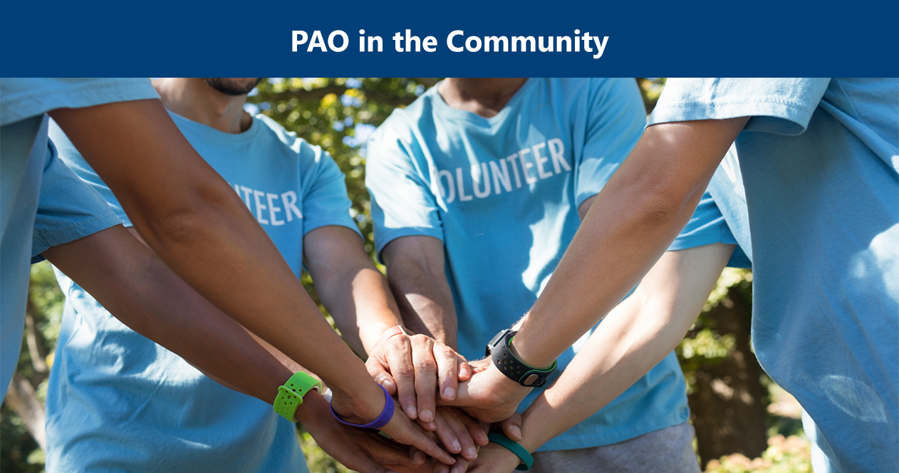 Image: A group of volunteers holding all hands in the center of their circle.